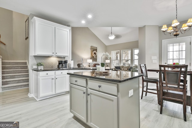 kitchen featuring pendant lighting, white cabinetry, a center island, decorative backsplash, and vaulted ceiling