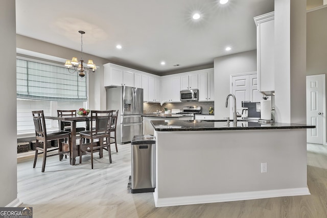 kitchen featuring appliances with stainless steel finishes, pendant lighting, white cabinetry, sink, and light hardwood / wood-style flooring