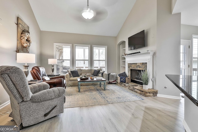 living room featuring built in shelves, a stone fireplace, vaulted ceiling, and light wood-type flooring