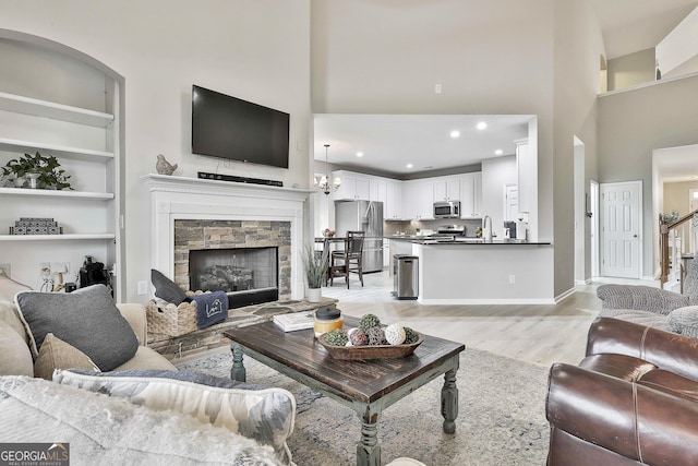 living room featuring a towering ceiling, built in features, a fireplace, sink, and light wood-type flooring