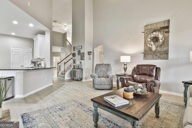 living room with a towering ceiling, sink, ceiling fan, and light hardwood / wood-style flooring