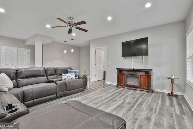 living room with ceiling fan, a fireplace, and light hardwood / wood-style floors