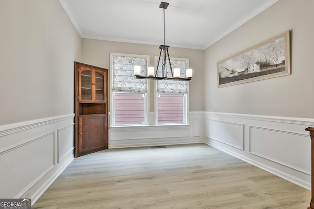 unfurnished dining area featuring an inviting chandelier, ornamental molding, and light hardwood / wood-style flooring