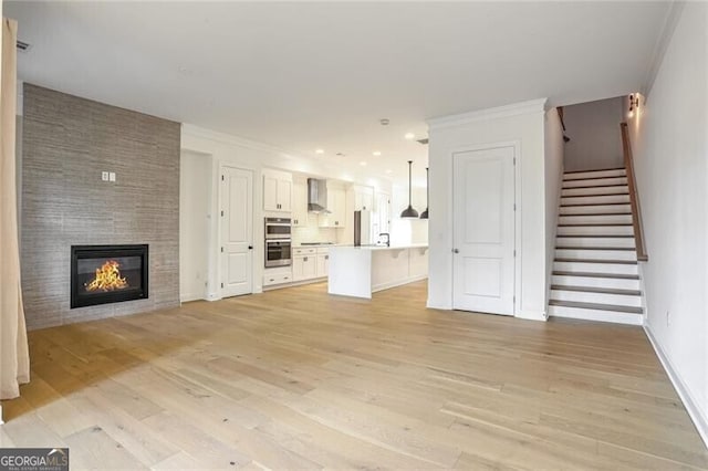 unfurnished living room featuring crown molding, a tiled fireplace, and light hardwood / wood-style floors