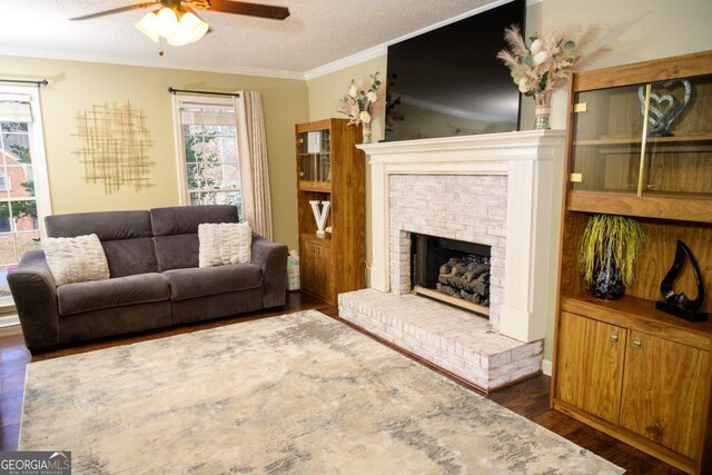 living room with dark hardwood / wood-style floors, a fireplace, ornamental molding, ceiling fan, and a textured ceiling