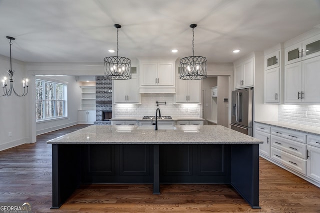 kitchen with sink, white cabinetry, high end refrigerator, a center island with sink, and light stone countertops