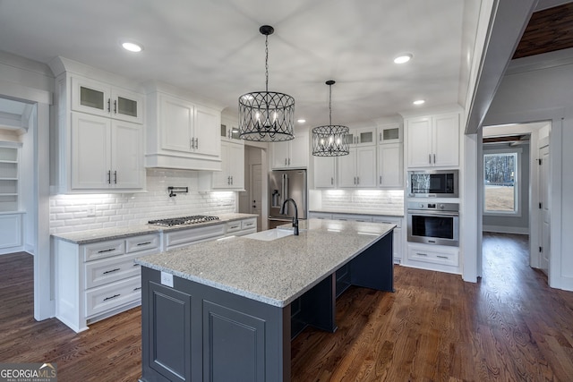 kitchen with appliances with stainless steel finishes, backsplash, an island with sink, white cabinets, and dark hardwood / wood-style flooring