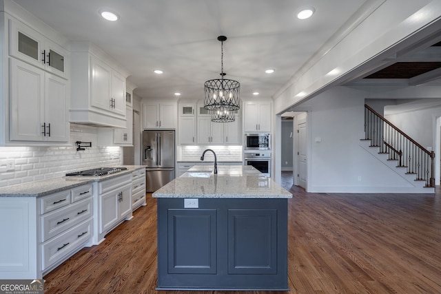 kitchen with stainless steel appliances, a kitchen island with sink, white cabinets, and light stone counters