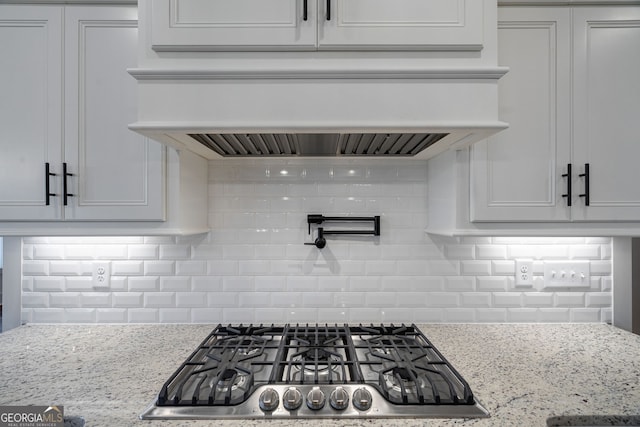 kitchen featuring stainless steel gas stovetop, premium range hood, light stone countertops, and decorative backsplash