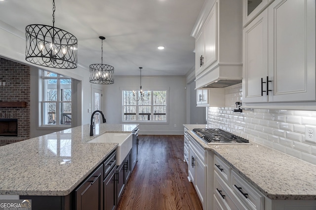 kitchen featuring a kitchen island with sink, sink, hanging light fixtures, and white cabinets