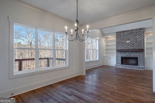 unfurnished living room featuring built in shelves, dark hardwood / wood-style flooring, an inviting chandelier, and a brick fireplace