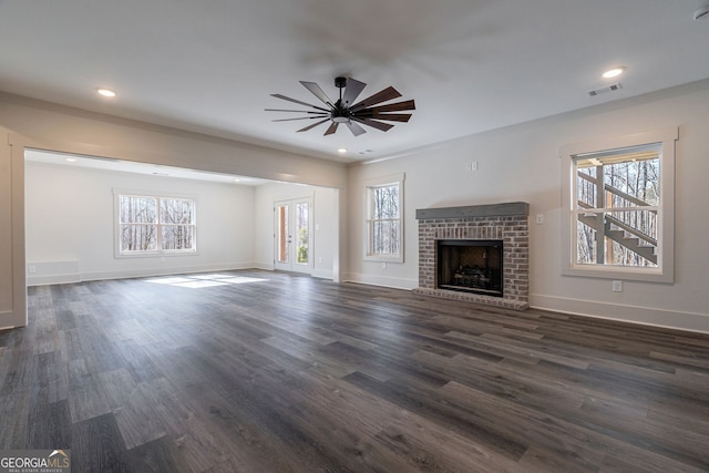 unfurnished living room featuring dark wood-type flooring, ceiling fan, ornamental molding, and a brick fireplace