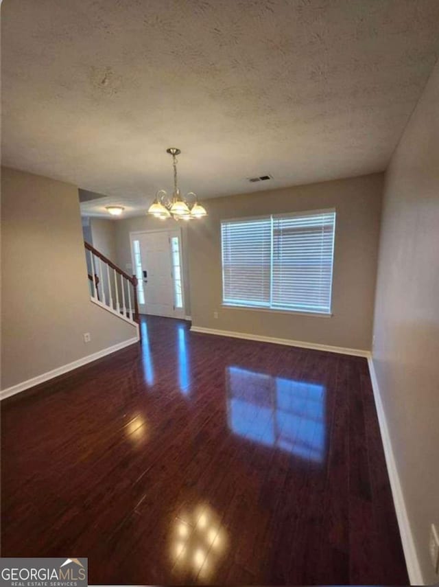 empty room with dark hardwood / wood-style floors, a textured ceiling, and a chandelier