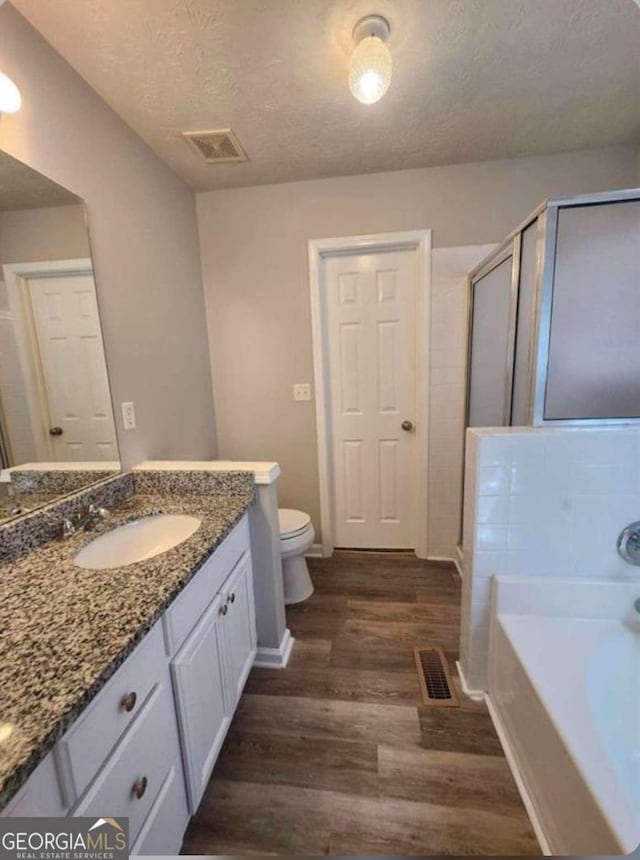 full bathroom with toilet, wood-type flooring, a textured ceiling, vanity, and plus walk in shower