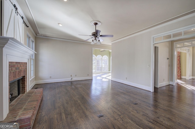 unfurnished living room featuring crown molding, a brick fireplace, dark wood-type flooring, and ceiling fan