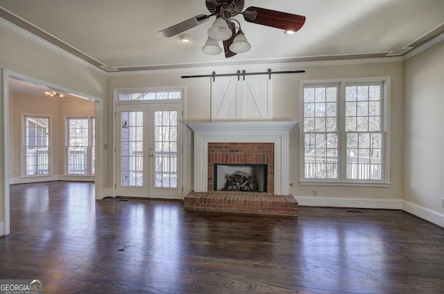 unfurnished living room featuring ceiling fan, crown molding, a brick fireplace, dark wood-type flooring, and french doors