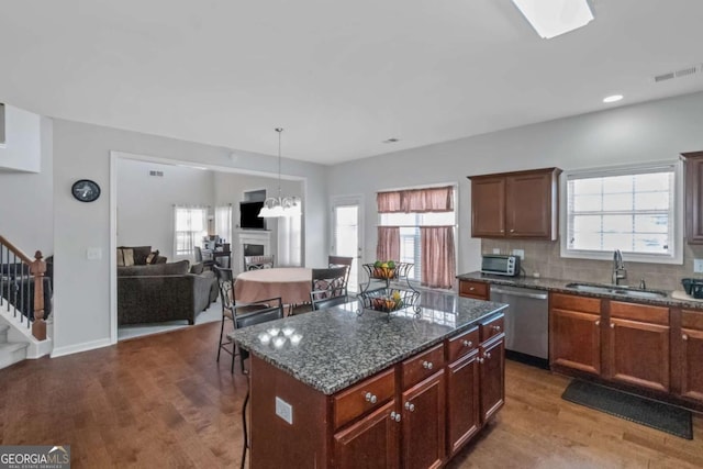 kitchen with sink, dark wood-type flooring, dark stone countertops, a kitchen island, and stainless steel dishwasher