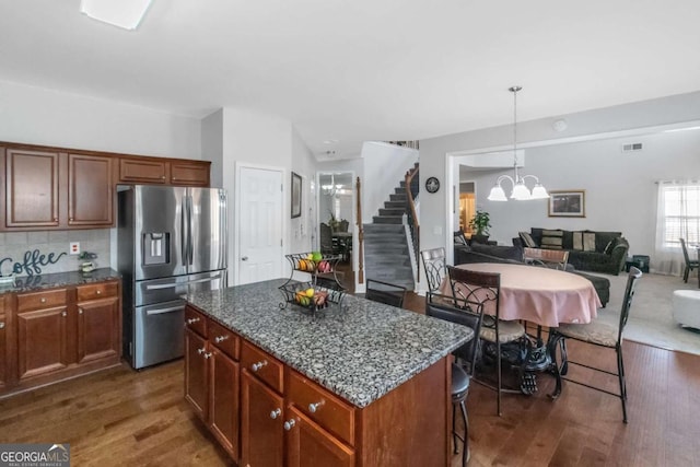 kitchen featuring a breakfast bar, an inviting chandelier, dark stone countertops, a center island, and stainless steel refrigerator with ice dispenser