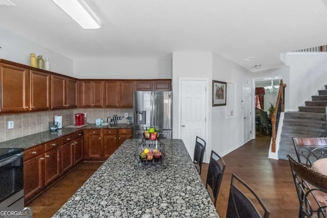 kitchen with decorative backsplash, dark hardwood / wood-style floors, stainless steel appliances, and dark stone counters