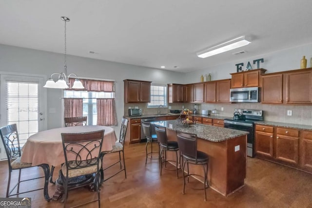 kitchen featuring appliances with stainless steel finishes, hanging light fixtures, a kitchen island, and backsplash