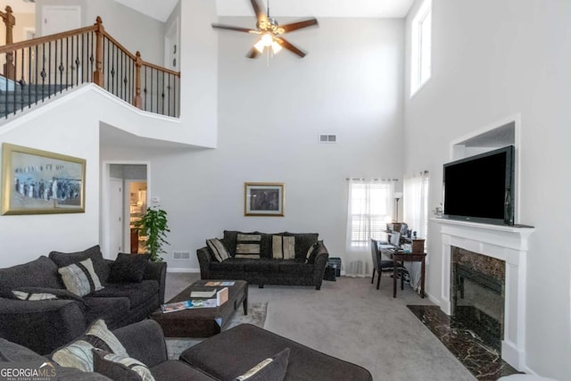 carpeted living room featuring ceiling fan, a fireplace, and a high ceiling