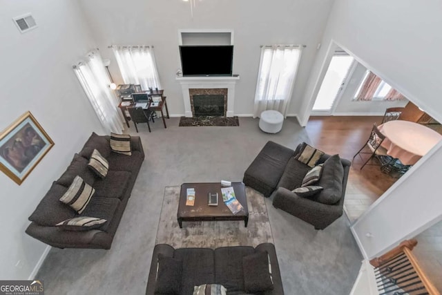 living room featuring a towering ceiling, a high end fireplace, and carpet floors