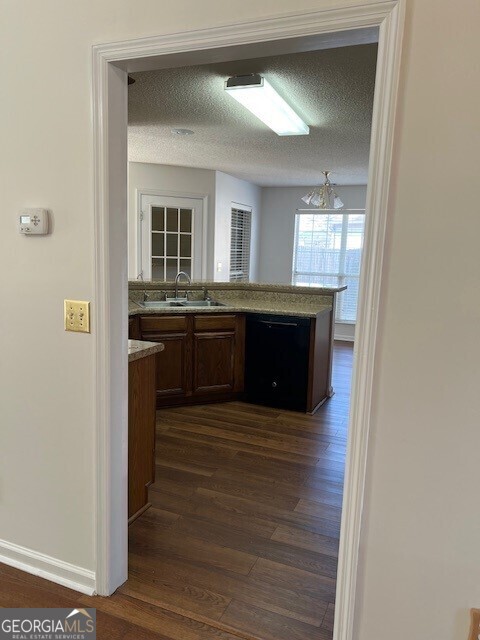 kitchen featuring sink, a textured ceiling, dark hardwood / wood-style floors, kitchen peninsula, and dishwasher