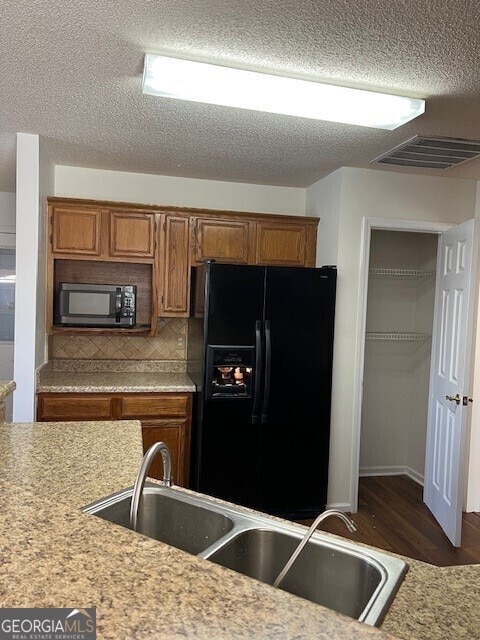 kitchen with sink, tasteful backsplash, black appliances, a textured ceiling, and dark hardwood / wood-style flooring