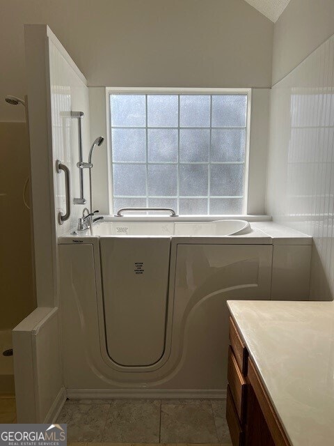 bathroom with lofted ceiling, tile patterned flooring, vanity, and a washtub