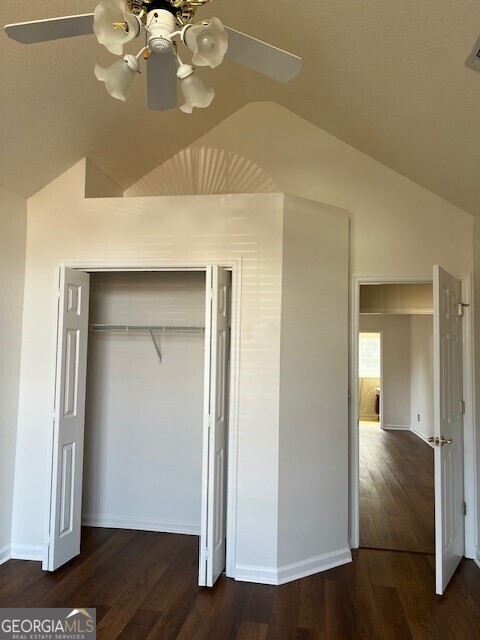 unfurnished bedroom with dark hardwood / wood-style flooring, vaulted ceiling, a closet, and ceiling fan