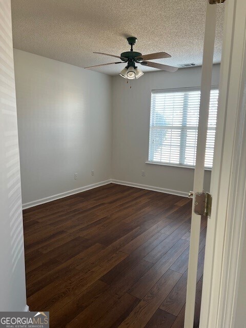 empty room with ceiling fan, dark hardwood / wood-style floors, and a textured ceiling