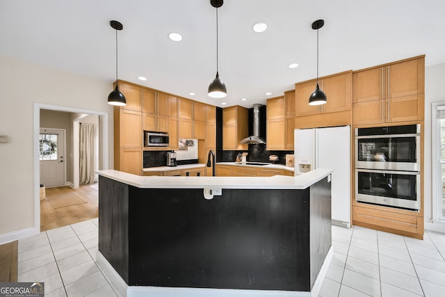 kitchen featuring stainless steel appliances, decorative light fixtures, a kitchen island with sink, and wall chimney range hood