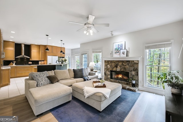 living room featuring ceiling fan, a fireplace, a healthy amount of sunlight, and light wood-type flooring