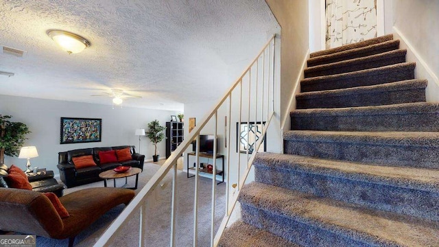 staircase featuring ceiling fan, carpet floors, and a textured ceiling