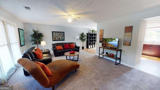 living room with ceiling fan, plenty of natural light, light colored carpet, and a textured ceiling