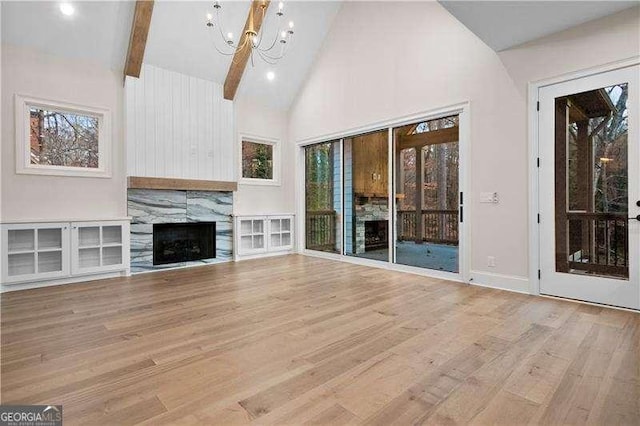 unfurnished living room with beam ceiling, high vaulted ceiling, a fireplace, a chandelier, and light wood-type flooring