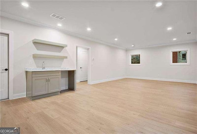 unfurnished living room with sink, crown molding, and light hardwood / wood-style floors