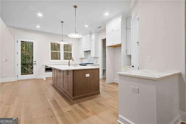 kitchen featuring pendant lighting, white cabinetry, light stone counters, light hardwood / wood-style floors, and an island with sink