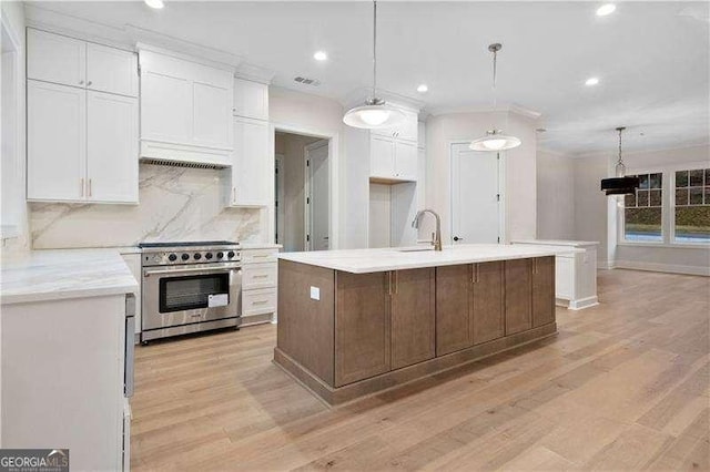 kitchen featuring white cabinetry, high end range, decorative light fixtures, a kitchen island with sink, and decorative backsplash