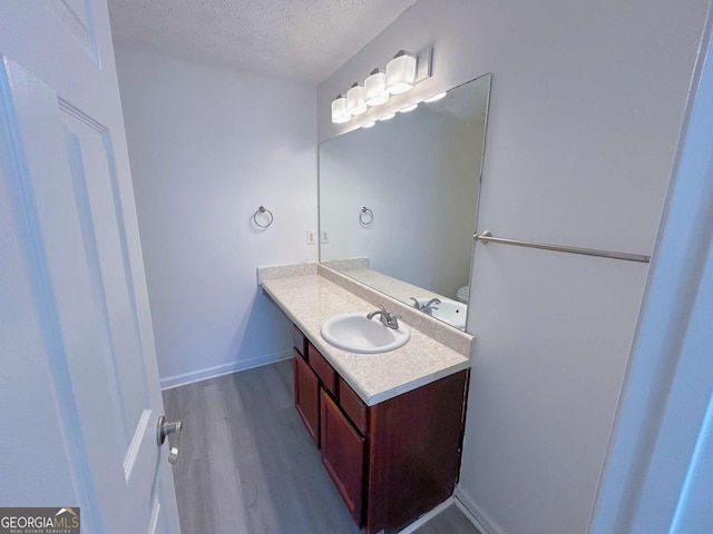 bathroom with baseboards, a textured ceiling, wood finished floors, and vanity