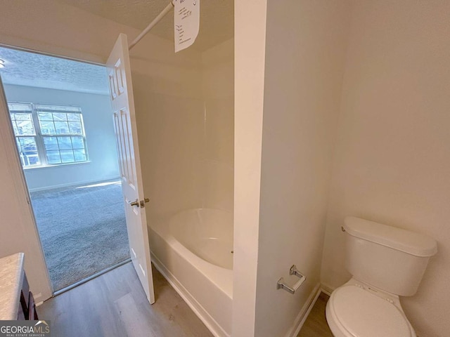 bathroom featuring toilet, wood finished floors, baseboards, and a textured ceiling