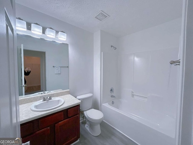 full bath featuring vanity, washtub / shower combination, visible vents, a textured ceiling, and toilet