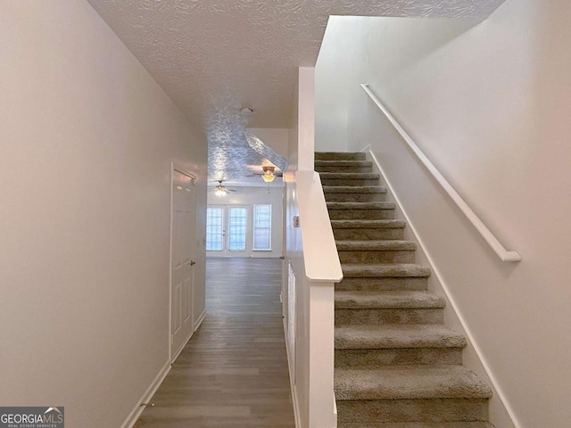 stairs featuring ceiling fan, wood finished floors, baseboards, and a textured ceiling