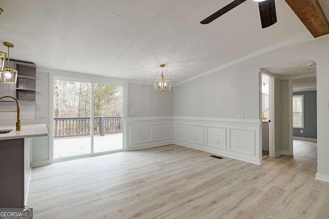 unfurnished dining area with a textured ceiling, sink, light hardwood / wood-style flooring, and a wealth of natural light