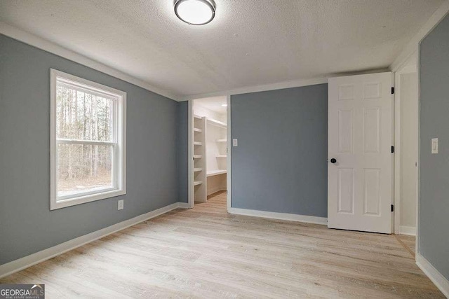 unfurnished bedroom with a walk in closet, a textured ceiling, light hardwood / wood-style floors, and a closet