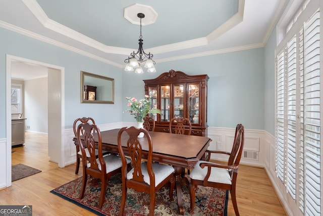 dining space with a raised ceiling, ornamental molding, an inviting chandelier, and light hardwood / wood-style floors