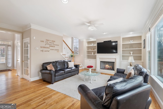 living room with built in features, ornamental molding, a high end fireplace, light hardwood / wood-style floors, and french doors