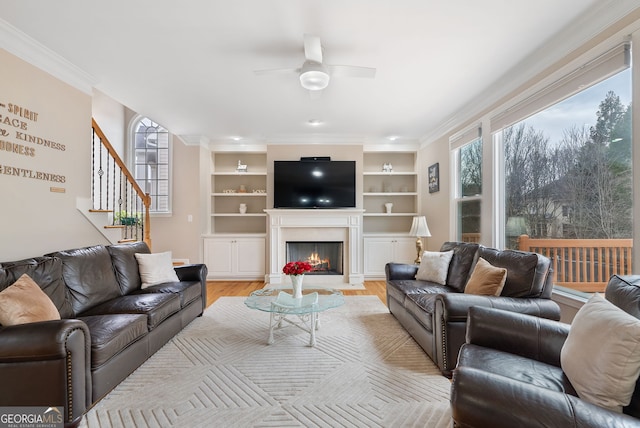 living room featuring built in shelves, light hardwood / wood-style flooring, ornamental molding, and ceiling fan