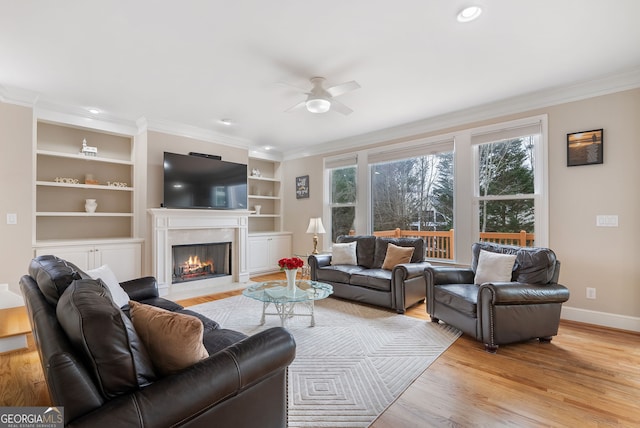 living room with crown molding, light wood-type flooring, built in features, ceiling fan, and a high end fireplace