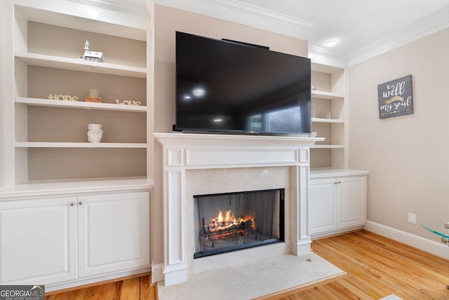 unfurnished living room with crown molding, a premium fireplace, built in shelves, and light wood-type flooring